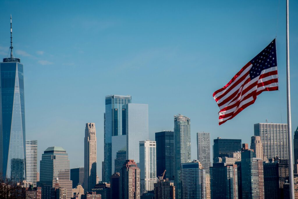 pexels-photo-7136320-7136320 Iconic New York City skyline with American flag flying under clear blue sky.